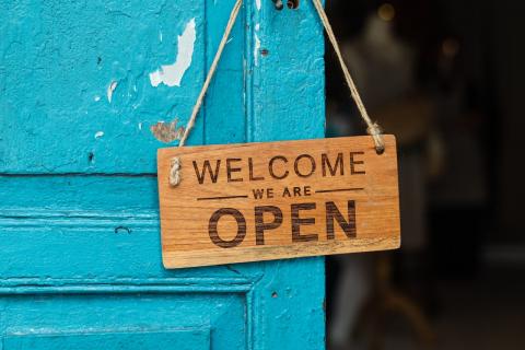 A blue door, from which hangs a wooden sign reading "welcome, we are open"